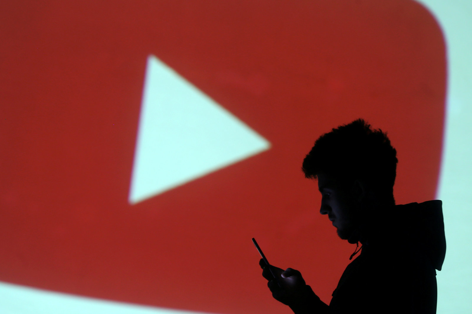 A silhouette of a mobile user is seen next to a screen projection of Youtube logo in this picture illustration taken March 28, 2018.  REUTERS/Dado Ruvic/Illustration