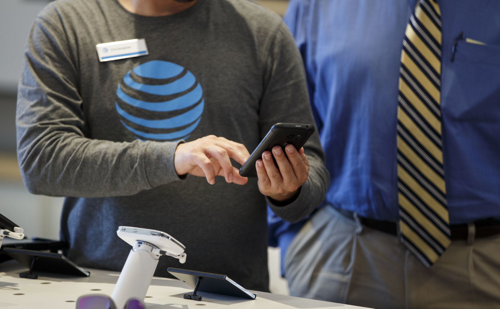 An employee helps a customer with a smartphone at an AT&T Inc. store in Newport Beach, California, U.S., on Thursday, Aug. 10, 2017. AT&T Inc. shares surged the most in more than eight years after the telecommunications giant posted a surprise wireless subscriber gain in the second quarter, showing it can fend for itself in a cutthroat price war. An offer for unlimited wireless data, bundled with discounted streaming-TV service, helping AT&T bide its time while awaiting regulatory approval to transform into a media powerhouse through the $85.4 billion purchase of Time Warner Inc. Photographer: Patrick T. Fallon/Bloomberg via Getty Images