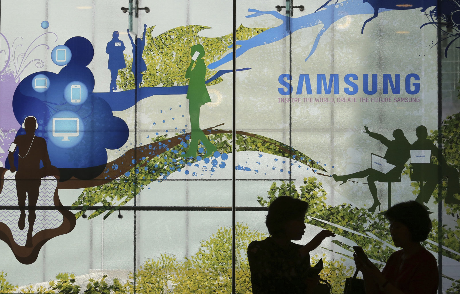 Visitors are silhouetted at Samsung Electronics shop in Seoul, South Korea, Friday, July 5, 2019. Samsung Electronics Co. said Friday its operating profit for the last quarter likely fell more than 56% from a year earlier amid a weak market for memory chips. (AP Photo/Ahn Young-joon)